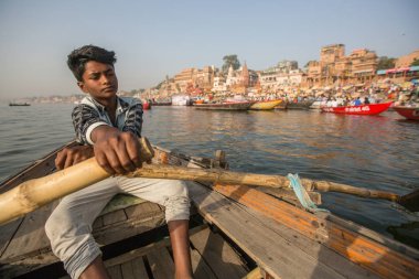 Varanasi, Hindistan - 26 Mar 2018: Bir teknede Boatmen Varanasi kıyı boyunca Ganj Nehri üzerinde suyun içinden süzülüyor. Efsaneye göre Varanasi Tanrı Shiva tarafından 5000 yıl önce kurulmuş.