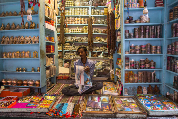 VARANASI, INDIA - MAR 23, 2018: Seller on the banks of the sacred Ganges river selling souvenirs in his street shop.