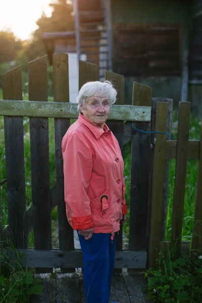 Yaşlı bir kadın bir köy evinin çitin dur. Kırsal yaşam.