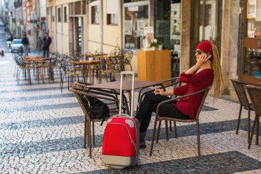 Kadın açık bir kafede bir masada oturan telefonda konuşurken kırmızı çanta.