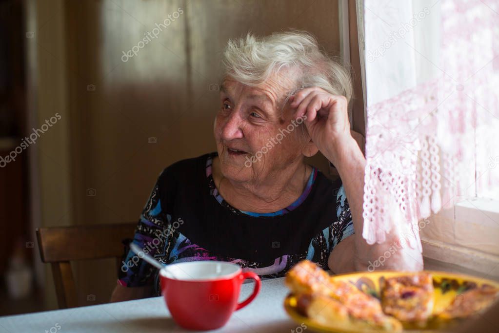 An elderly woman sitting at the table drinking tea with pies.