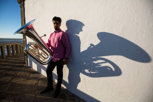 Man with Tuba musical instrument near the white wall the shadow of the tool.