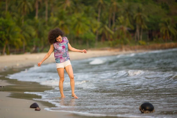 Tropikal deniz sahilde yürüyen genç karışık ırk kadın.
