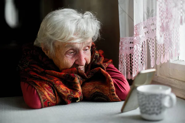 坐在桌前看着智能手机屏幕的老妇人 — 图库照片