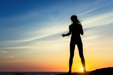 Muhteşem gün batımı sırasında deniz kıyısında genç kadın silüeti. 