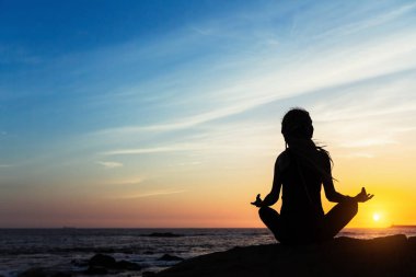 Yoga kadın siluet deniz sahilde günbatımı sırasında yapıyor. 