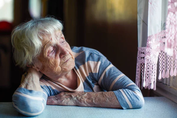 一个年老的女人悲伤地坐在窗边 — 图库照片