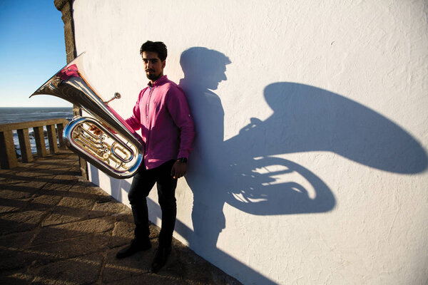 Man play Tuba near the white wall the shadow of the tool. 