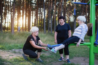 Yaşlı kadın spor simülatör Park iki yetişkin kadın egzersizleri yapması için yardım. 