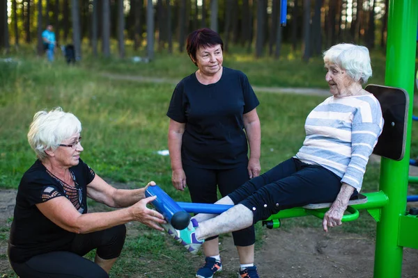 公園でスポーツのシミュレータの高齢女性は つの大人の女性を助ける彼女の演習を行う — ストック写真