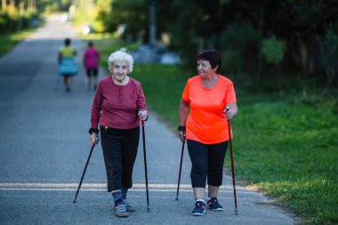 Yaşlı bir kadın yetişkin kızıyla birlikte Nordic walking ın devreye.