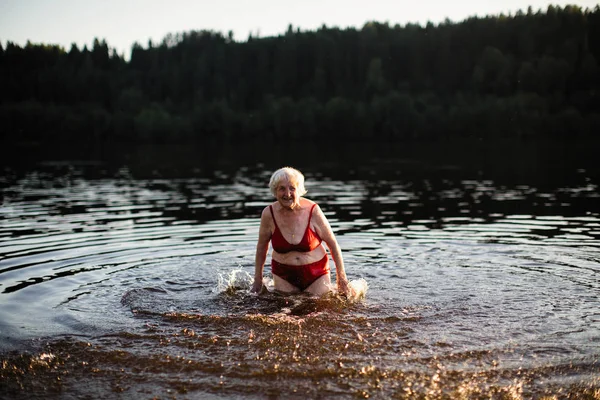 An elderly woman is having fun swimming in the river.