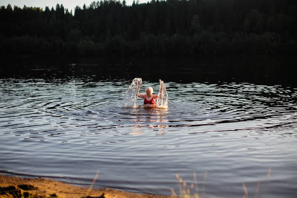 An elderly woman is having fun swimming in the river.