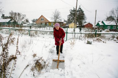 Yaşlı kadın temizler kar onun yakınındaki kırsal vinter evinde.