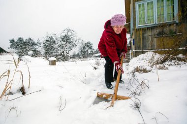 Yaşlı kadın temizler kar onun yakınındaki kırsal vinter evinde.