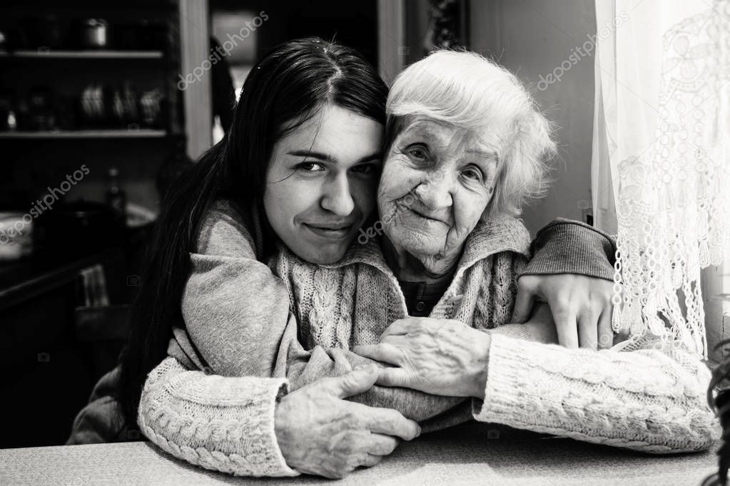 Elderly woman in an embrace with an adult granddaughter in a village house. Black and white photo.