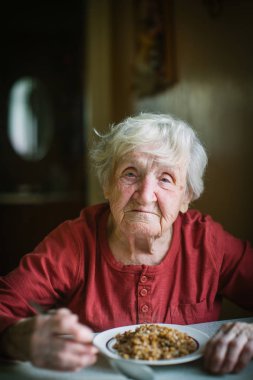 Yaşlı bir kadın oturma masada yiyor..