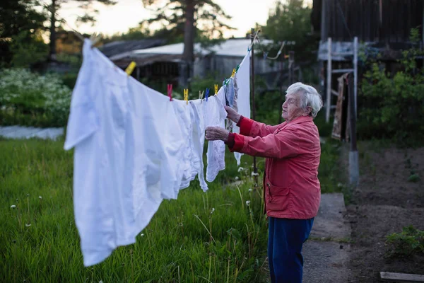 高齢者の女性彼の村の家の庭に洗った服をハングアップします — ストック写真