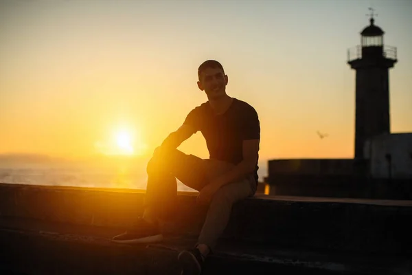 年轻男子坐在海滨长廊在日落 — 图库照片