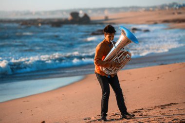 Musician instrumentalist playing the Tuba on the sea coast.  clipart