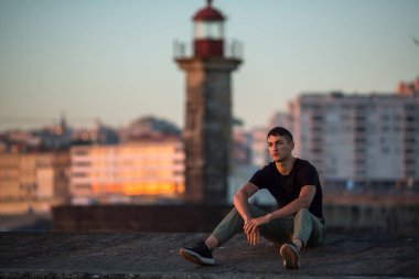 Deniz fenerinde gezinti günbatımı zaman üzerinde oturan genç adam.