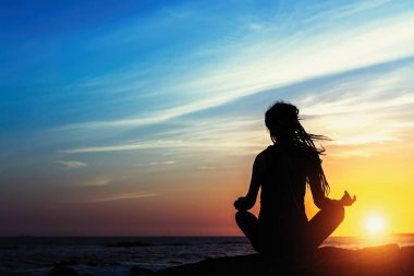 Gün batımında sahilde Yoga uygulamak siluet genç meditasyon kadın. 