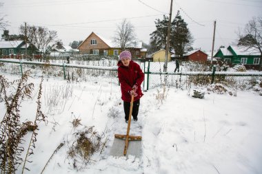 Yaşlı bir kadın evinin yakınında kar temizler.