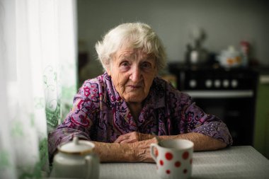 Masada oturan yaşlı bir kadın portresi.