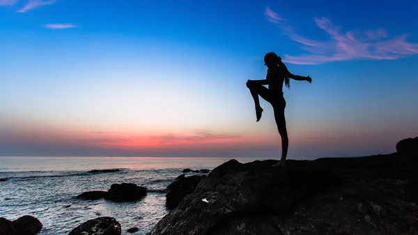 Silhouette of young gymnastics woman doing exercises on the Sea during amazing sunset.