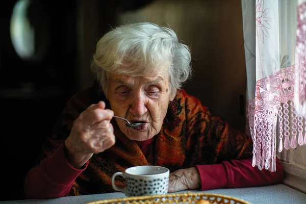 一位退休的老年妇女坐在家里喝勺子里的茶 — 图库照片