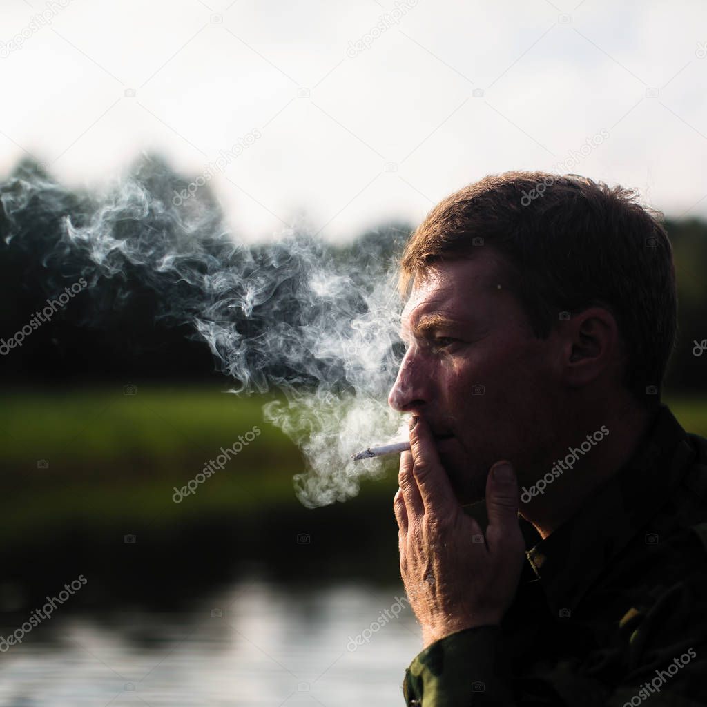 Man smoking outdoor, close-up. Smoke in the background light.