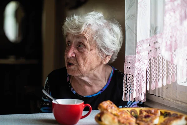 退休的老年妇女坐在他家的厨房里坐在桌旁 — 图库照片
