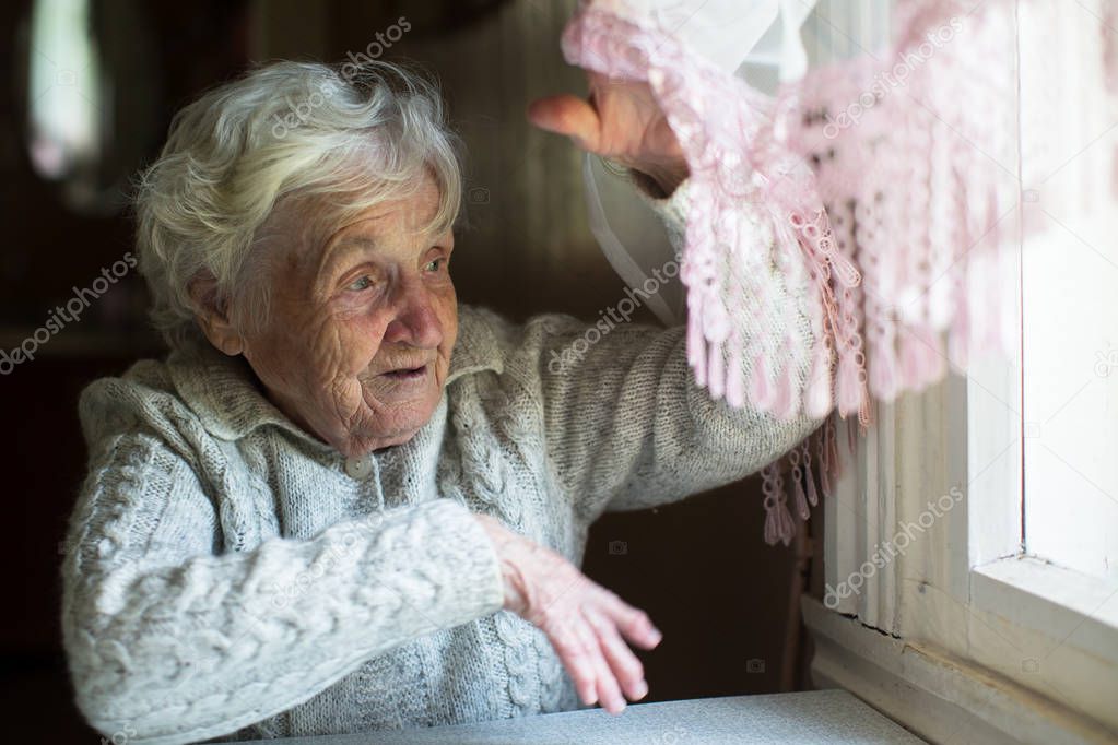 Gray-haired elderly woman looks out the window.