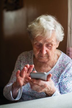Yaşlı kadın bir smartphone ile onun elinde oturur..