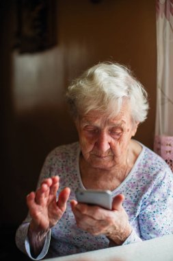 Yaşlı kadın bir smartphone ile onun elinde oturur.