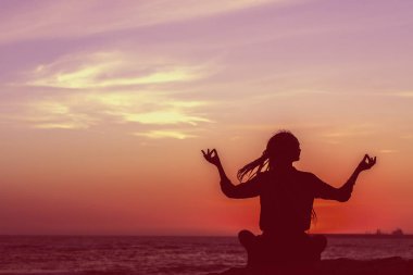 Yoga kadın meditasyon solmuş fotoğraf silüeti gün batımında sahilde.