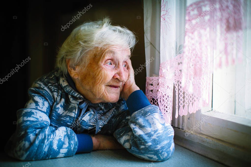 Elderly woman in the house sitting at the table looking out the window. 
