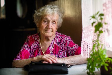 Bir masada oturan yaşlı kadın portresi.