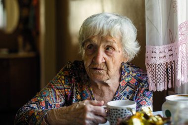 Yaşlı kadın masada oturup çay içme.