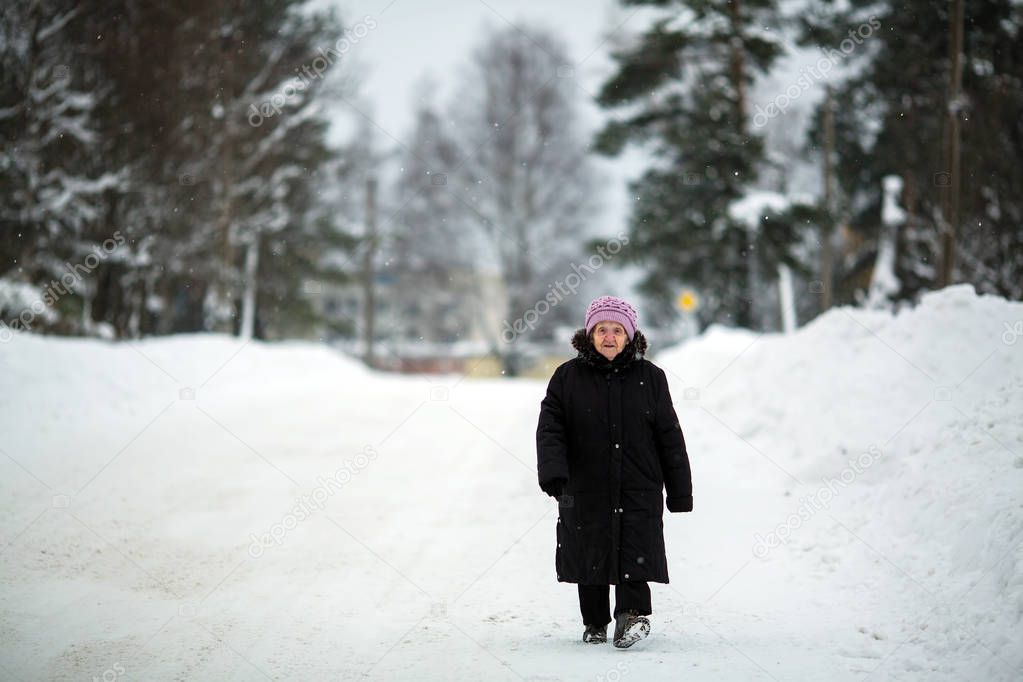 An elderly pensioner woman walking along the snowy winter street of the village.