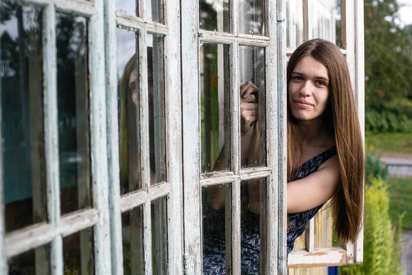 Genç kadın uzun saçlı pencereden görünüyor.