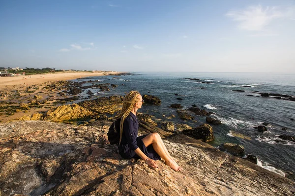 一个年轻的女人 金发碧眼的头发在岩石上看着大海 — 图库照片
