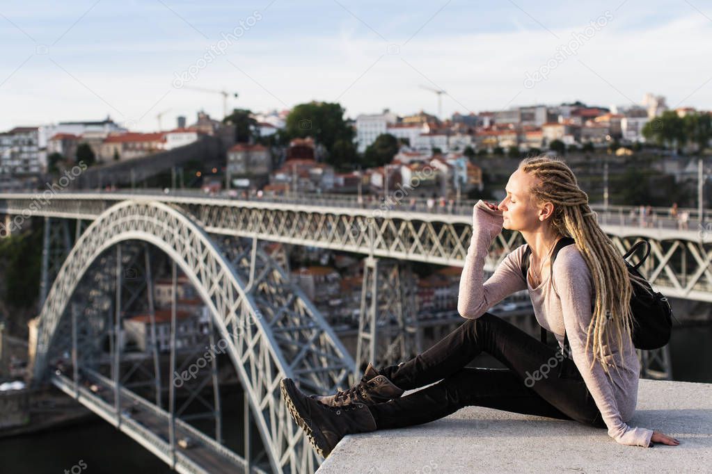 Young woman with dreadlocks sitting near bridge of Dom Luis I, Porto, Portugal.