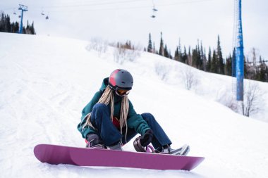 Kadın Snowboard botları kadar karlı bir yamaçta otururken sıkıştırma.