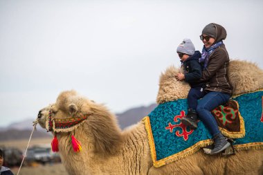 Sagsay, Moğolistan - Eyl 30, 2017: Yerel kazak kadın çocuk bir deve üzerinde yerel bir tatil sırasında rides. 