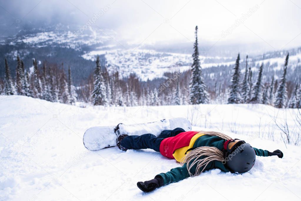Female snowboarder freerider with snowboard in the mountains resting lying on the snowy slope.