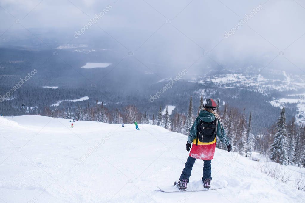 Female snowboarder freerider rides a snowboard on a snowy slope.