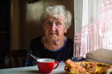 Yaşlı bir kadın evinin masada oturan mutfakta.