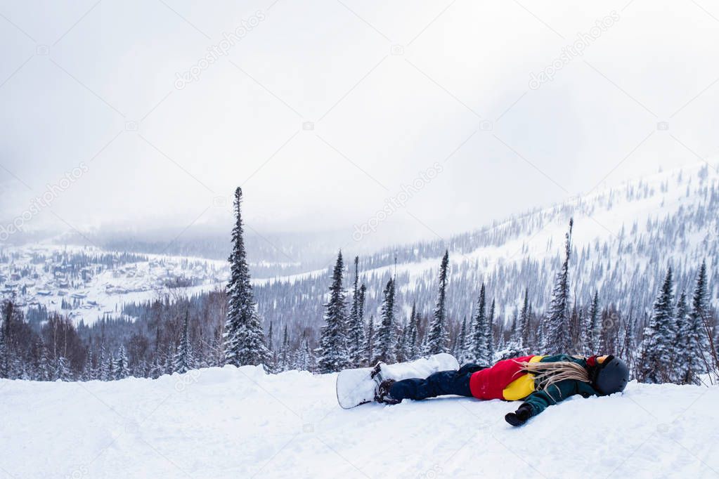 Female snowboarder with a snowboard lies in the mountains among the christmas trees under the snow. 