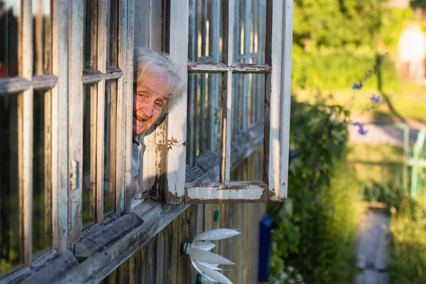 Μια Ηλικιωμένη Γυναίκα Κοιτάζει Από Παράθυρο Ενός Χωριού — Φωτογραφία Αρχείου